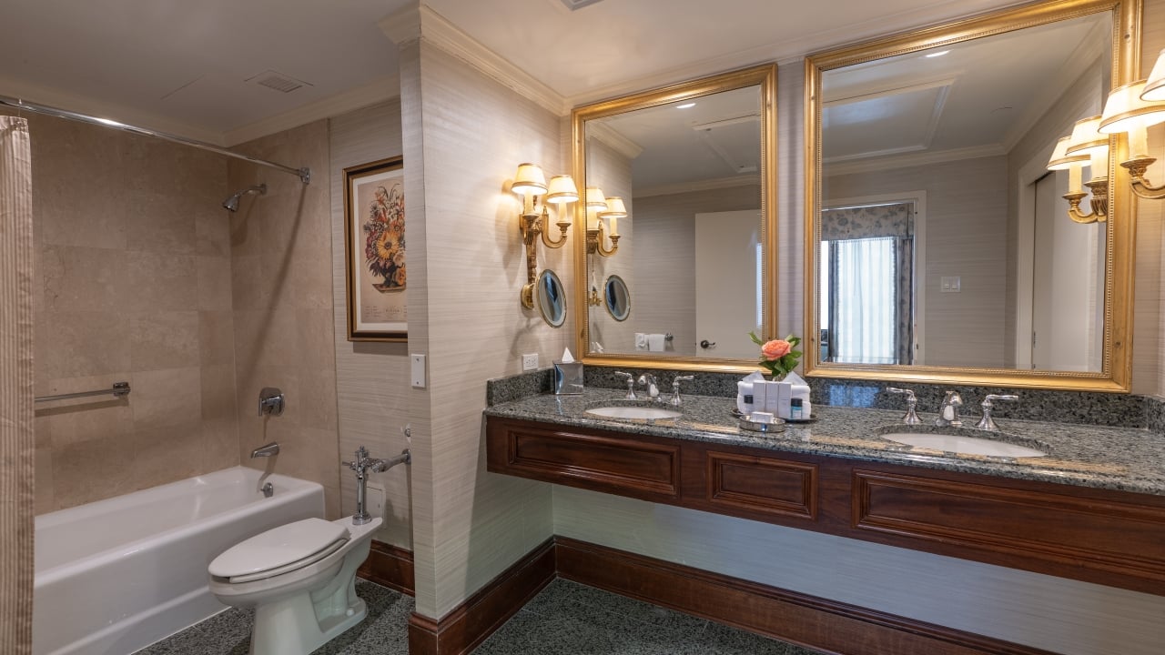 A luxurious bathroom with a double vanity, large mirrors, a tub/shower, and a toilet.