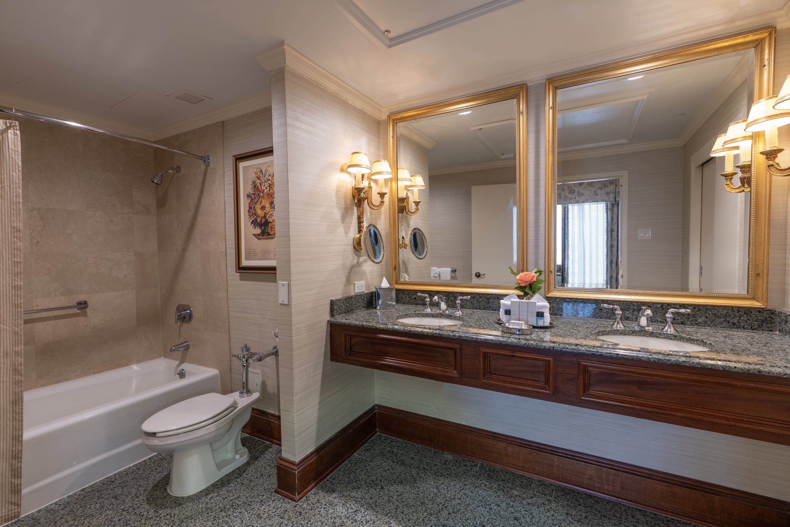 New Orleans hotel bathroom with a double vanity, elegant gold mirrors, bathtub, and guest amenities.