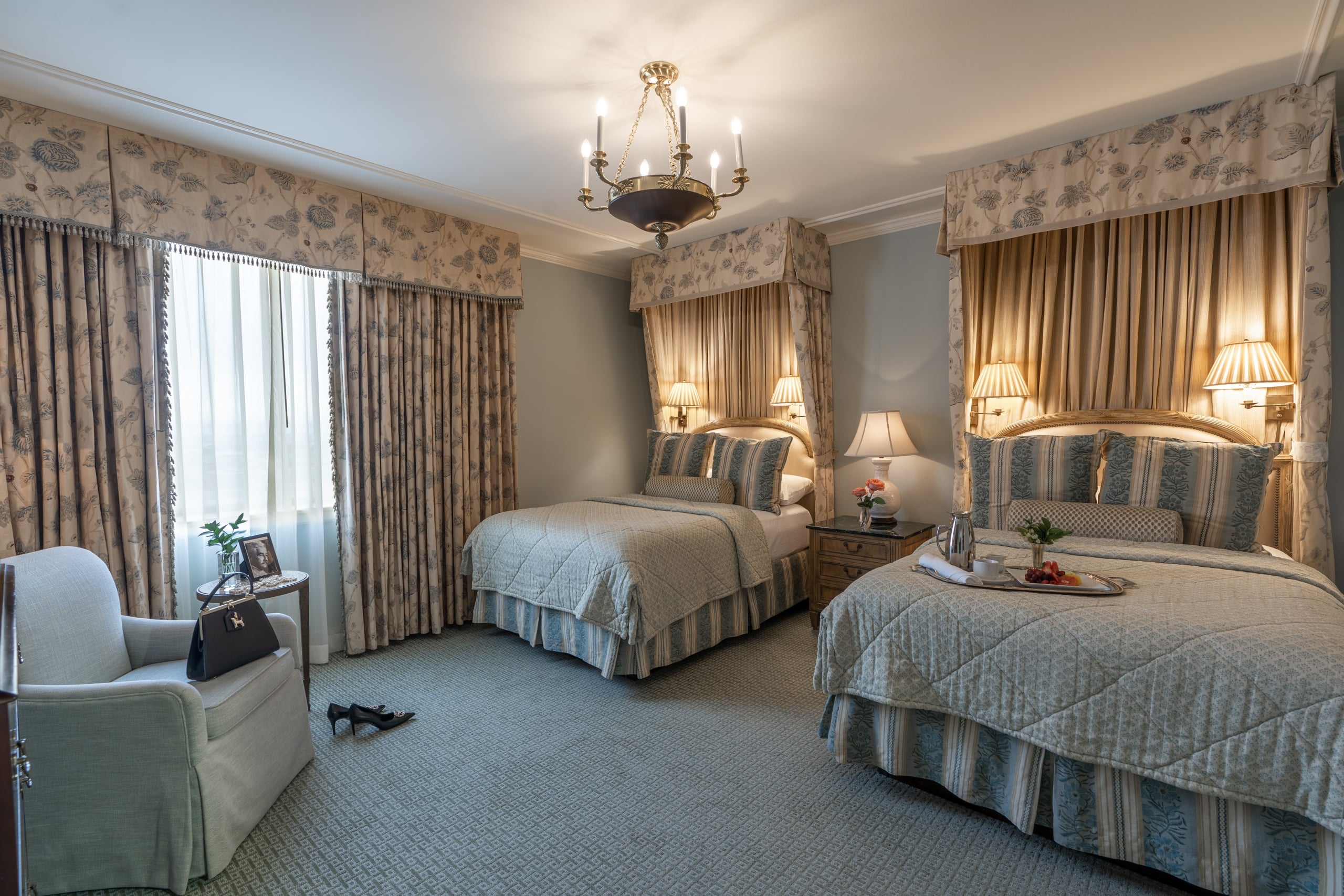 Luxury New Orleans hotel room with two beds, floral curtains and valances, and an ornate chandelier.
