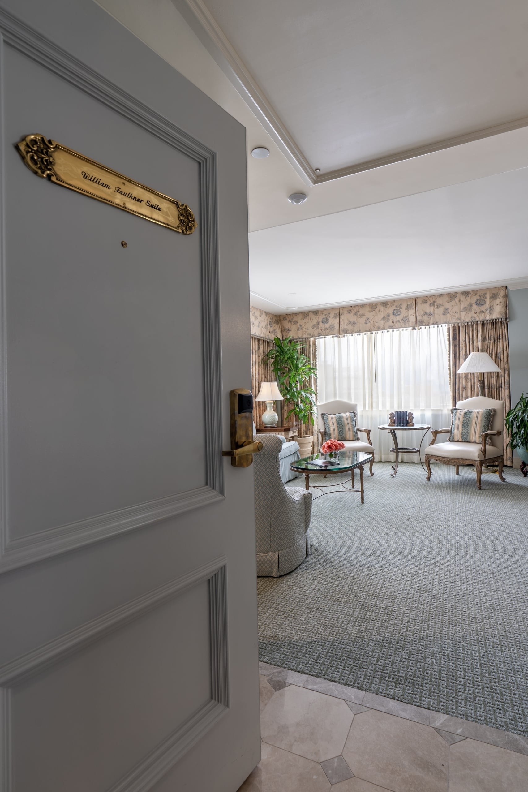William Faulkner Suite entrance showing an elegant living area with classic armchairs and patterned curtains.