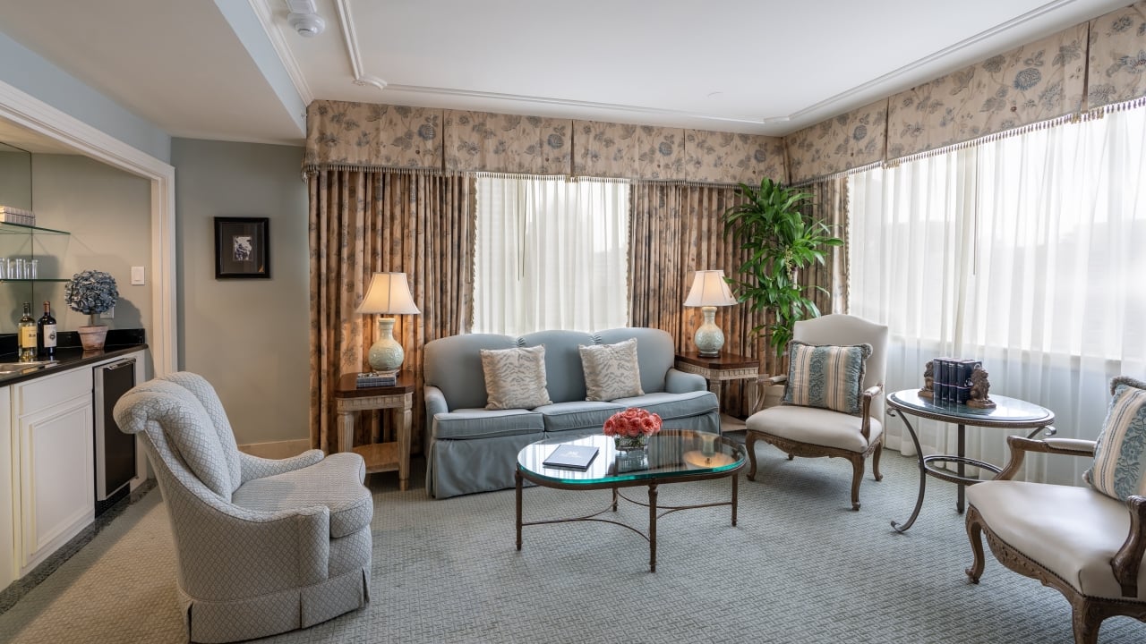 A wide view of a luxurious suite with a sofa, armchairs, coffee table, and kitchenette.