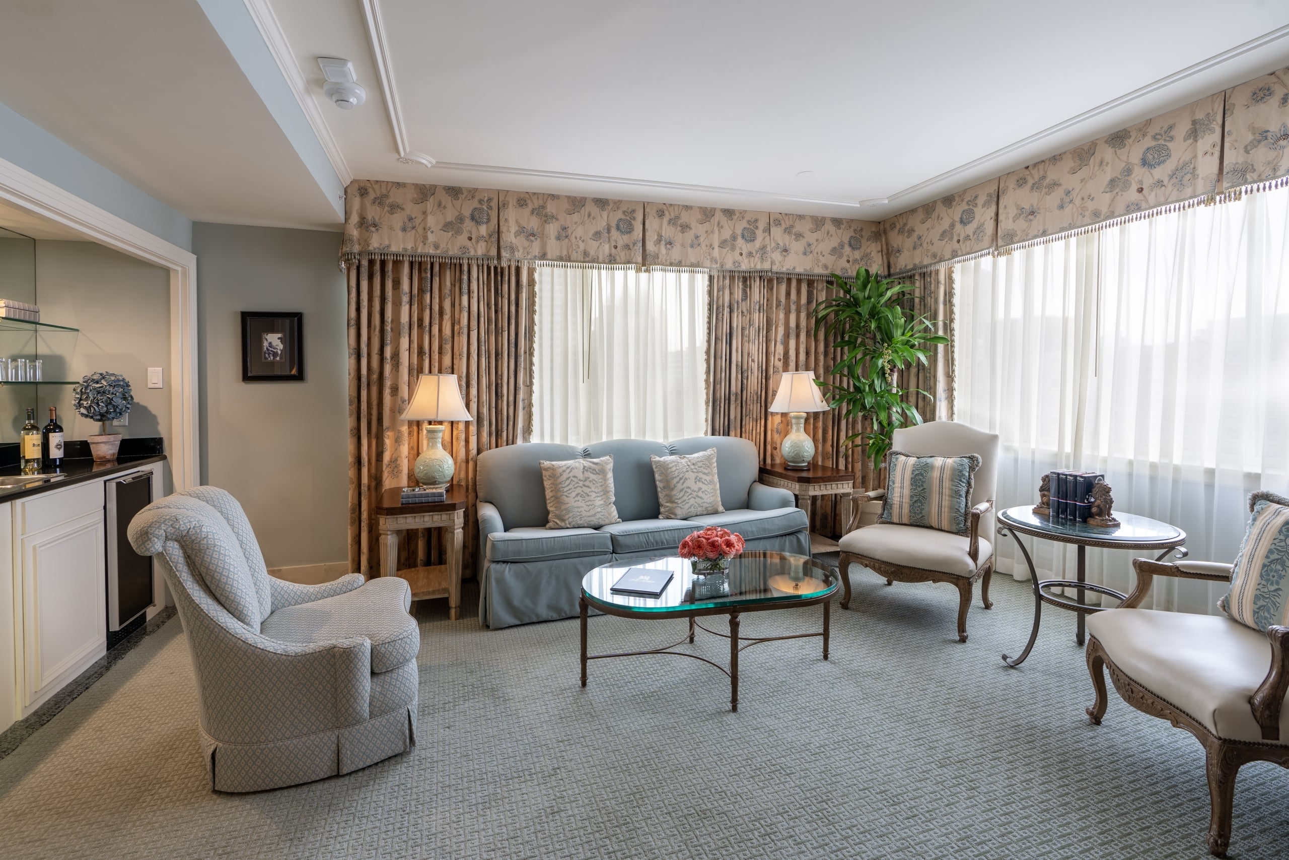 Luxurious New Orleans hotel suite living room with classic blue sofa, elegant armchairs, and a convenient wet bar.