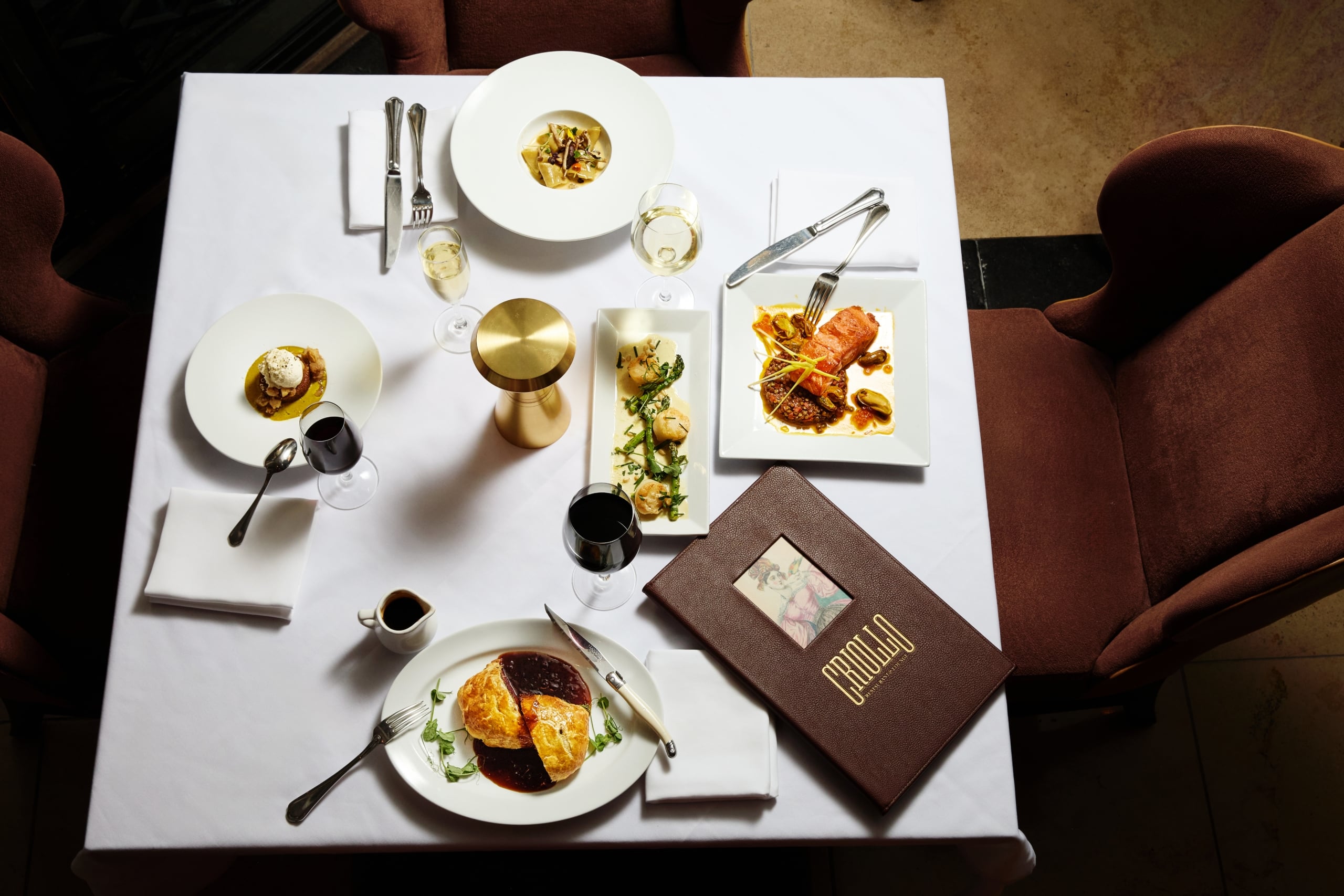 Table set for a gourmet meal with multiple elegant dishes, wine, and the Crillo Restaurant menu.