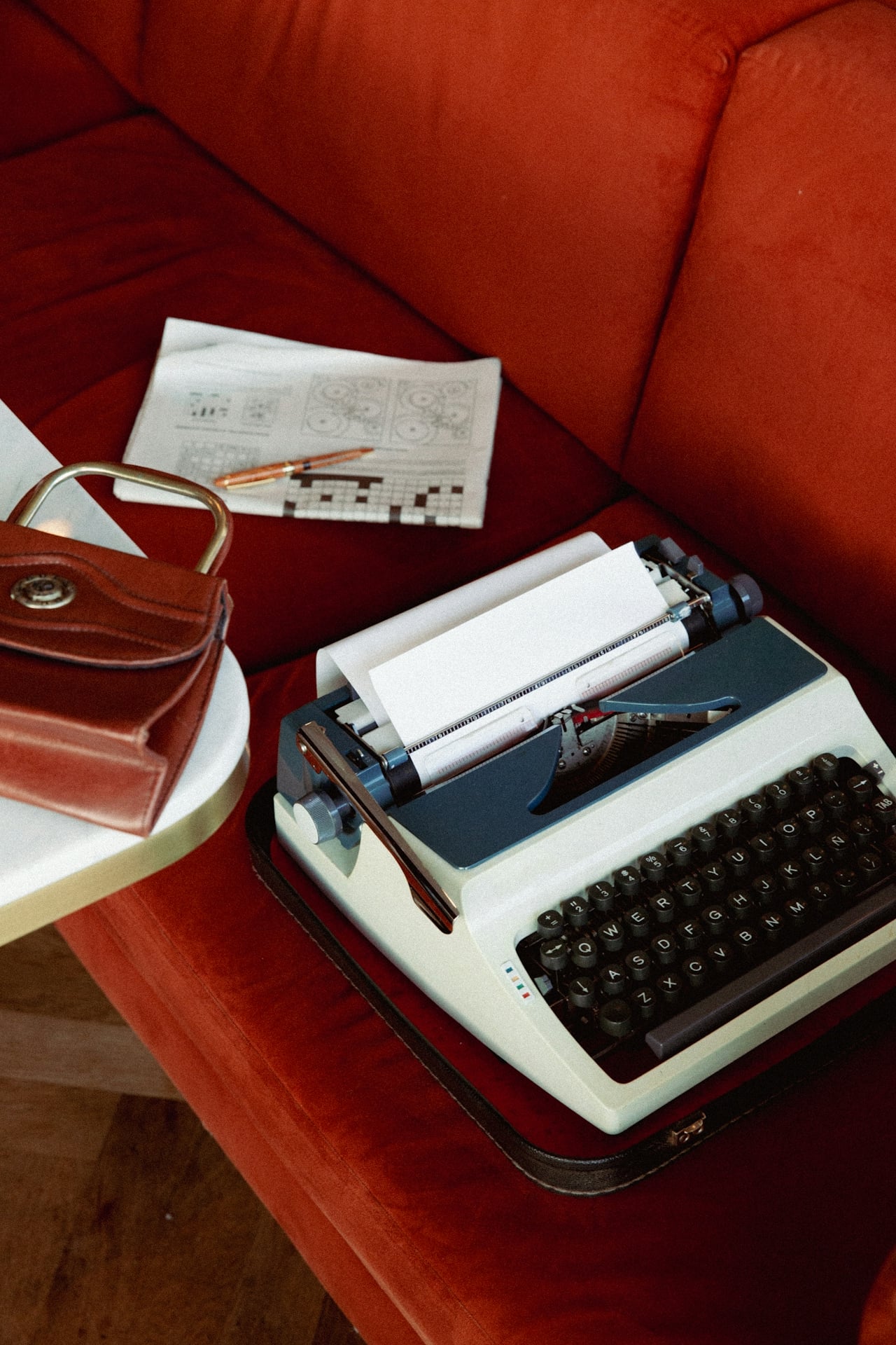 Vintage typewriter, crossword, and leather bag on a red sofa, evoking a relaxing New Orleans stay.