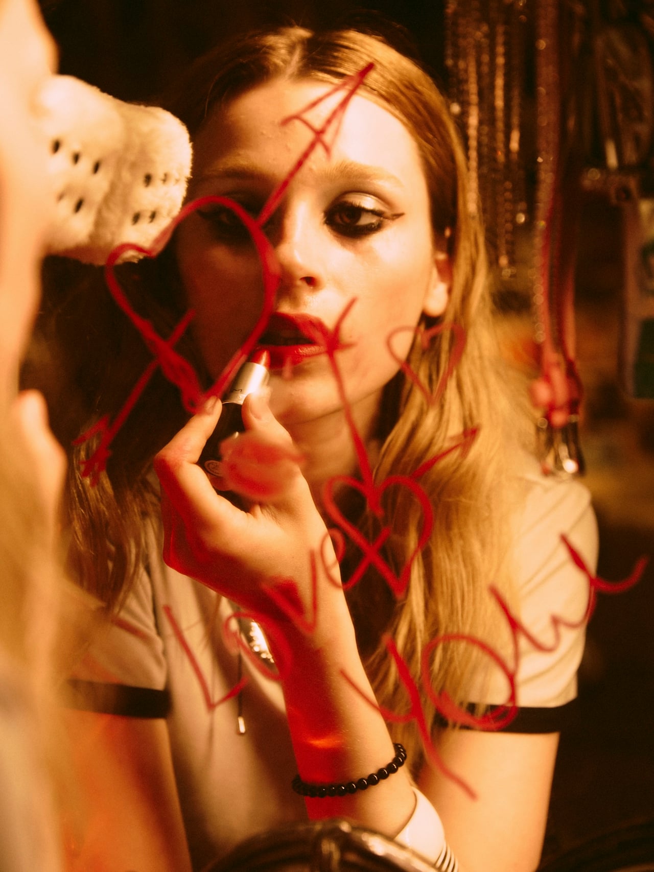 A woman applying red lipstick in a mirror with red hearts and 